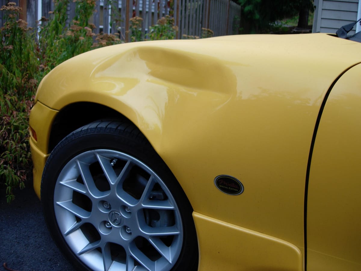 A picture of a yellow Miata with a big dent in the front fender